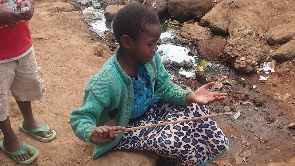 a young girl plays with the contents of a drain in the slums, a health hazard containing all sorts of waste including faeces